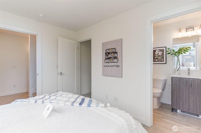 bedroom featuring a sink, light wood-type flooring, baseboards, and ensuite bath