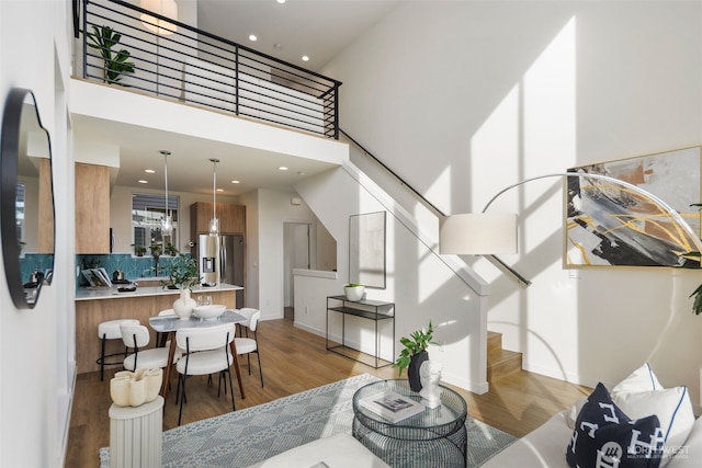 living area featuring light wood-type flooring, stairway, baseboards, and a high ceiling