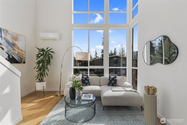 living room with a towering ceiling, wood finished floors, baseboards, and a wall mounted air conditioner