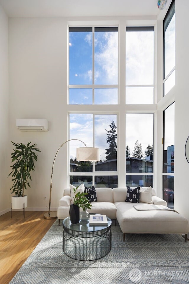 living room with baseboards, an AC wall unit, wood finished floors, and a towering ceiling