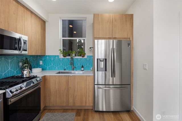 kitchen featuring modern cabinets, a sink, tasteful backsplash, stainless steel appliances, and light countertops