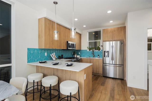 kitchen featuring brown cabinets, a sink, tasteful backsplash, stainless steel appliances, and a peninsula