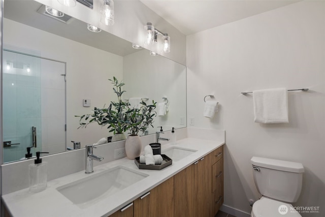 full bath featuring double vanity, toilet, a shower with shower door, and a sink