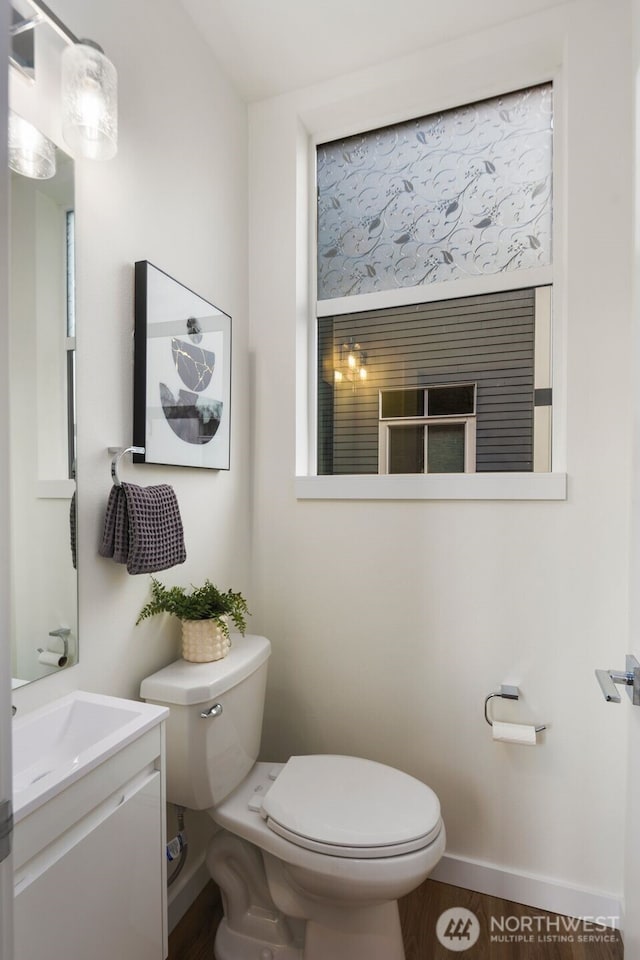 half bath featuring vanity, toilet, wood finished floors, and baseboards