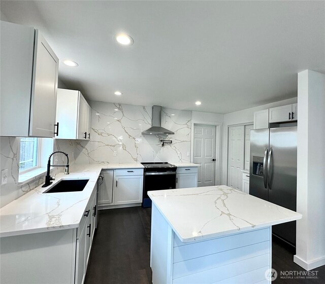 kitchen with light stone counters, range with electric stovetop, stainless steel fridge, wall chimney exhaust hood, and a sink