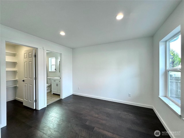 unfurnished bedroom with baseboards, recessed lighting, dark wood-style flooring, a walk in closet, and connected bathroom