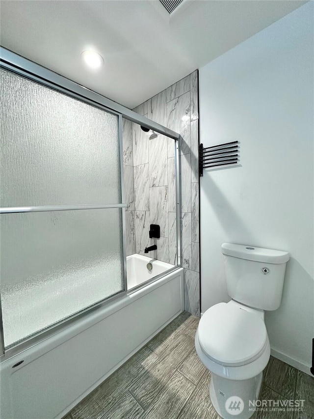 bathroom featuring baseboards, toilet, and shower / bath combination with glass door