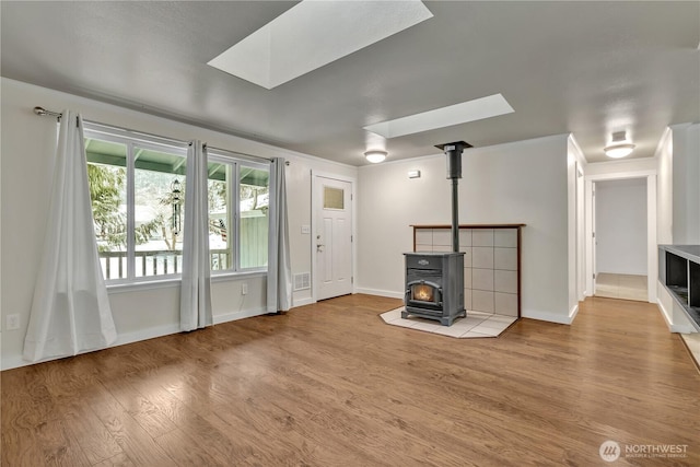 unfurnished living room featuring visible vents, light wood-style flooring, a skylight, baseboards, and a wood stove