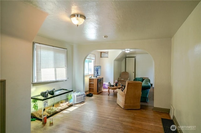 interior space with arched walkways, an AC wall unit, baseboards, and wood finished floors