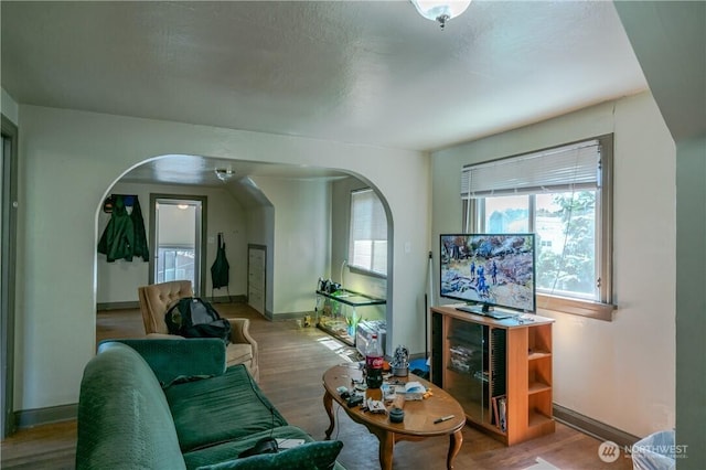 living area featuring baseboards, arched walkways, and wood finished floors