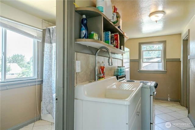 washroom with light tile patterned floors, laundry area, a sink, a textured ceiling, and washing machine and dryer