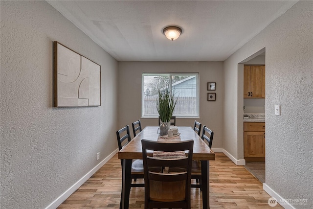 dining space with baseboards, light wood-style flooring, and a textured wall