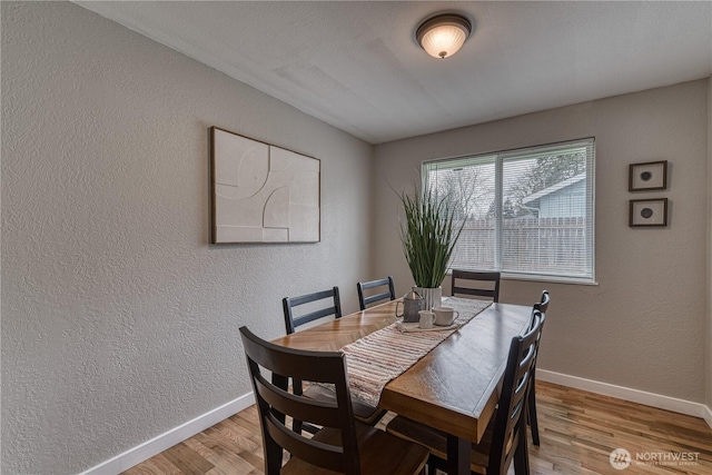 dining area with light wood-type flooring, baseboards, and a textured wall