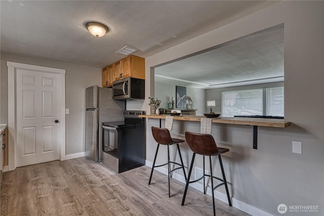 kitchen featuring wood finished floors, visible vents, baseboards, a breakfast bar, and appliances with stainless steel finishes