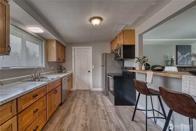 kitchen with light wood finished floors, stainless steel appliances, brown cabinetry, and a sink