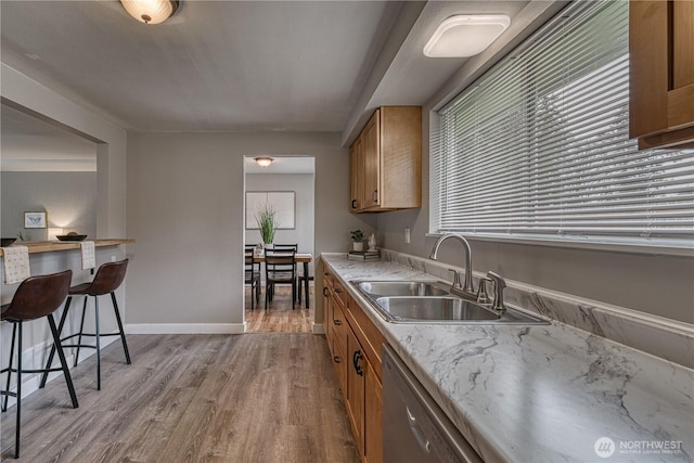 kitchen with dishwashing machine, brown cabinetry, light wood finished floors, and a sink