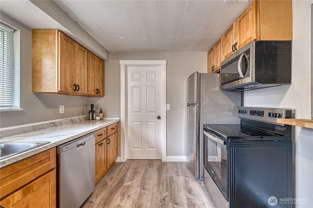 kitchen with brown cabinetry, light wood-style flooring, stainless steel appliances, and light countertops