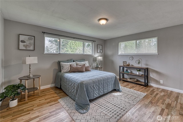bedroom with light wood-style floors, baseboards, and a textured ceiling