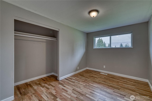 unfurnished bedroom with a closet, baseboards, visible vents, and wood finished floors