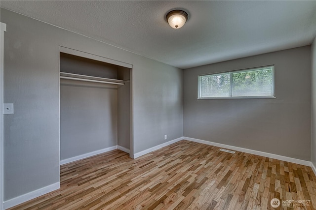 unfurnished bedroom featuring a closet, visible vents, baseboards, and wood finished floors