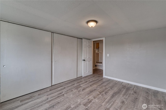 unfurnished bedroom with baseboards, wood finished floors, a closet, and a textured ceiling