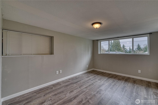 spare room with a textured ceiling, baseboards, and wood finished floors