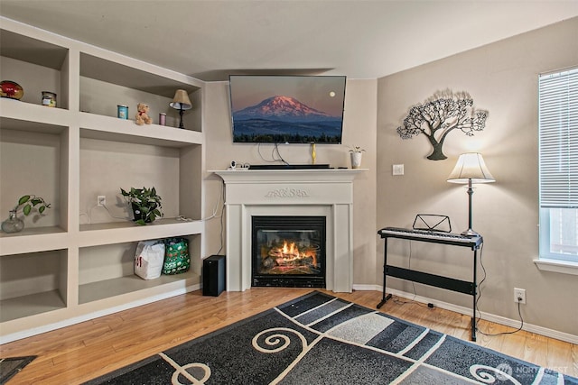 sitting room with built in features, baseboards, a glass covered fireplace, and wood finished floors