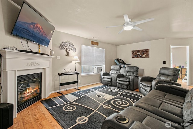 living room featuring a glass covered fireplace, baseboards, a ceiling fan, and wood finished floors