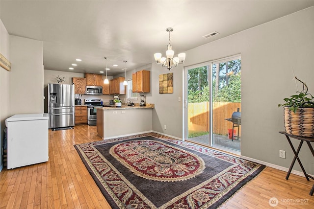 kitchen with light wood-type flooring, visible vents, appliances with stainless steel finishes, brown cabinetry, and a chandelier