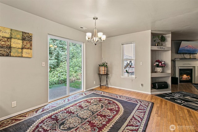 dining area with a glass covered fireplace, plenty of natural light, an inviting chandelier, and hardwood / wood-style flooring