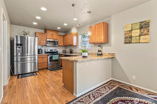 kitchen featuring a peninsula, light wood-style flooring, appliances with stainless steel finishes, pendant lighting, and brown cabinets