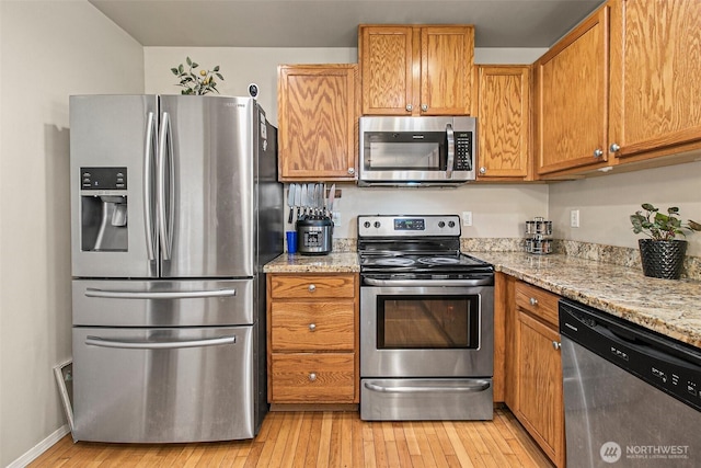 kitchen featuring light stone counters, light wood-style flooring, appliances with stainless steel finishes, and brown cabinets