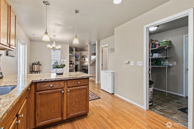 kitchen featuring brown cabinetry, an inviting chandelier, a peninsula, hanging light fixtures, and light wood-type flooring