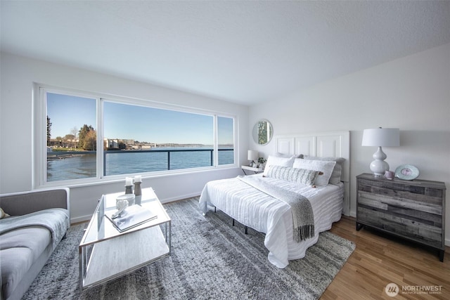 bedroom with baseboards, a water view, and wood finished floors