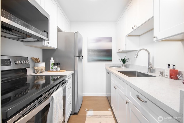 kitchen with a sink, light countertops, light wood-style floors, appliances with stainless steel finishes, and white cabinetry