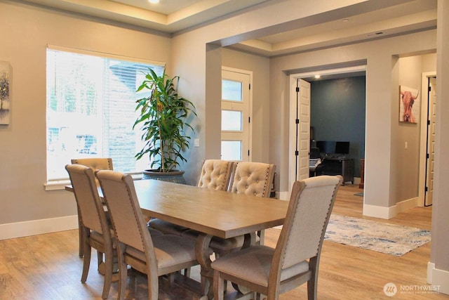 dining room featuring baseboards, a raised ceiling, and light wood-style flooring