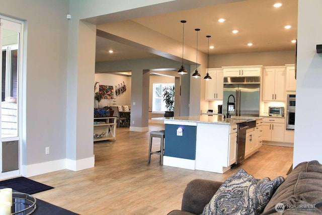 kitchen with white cabinets, light stone counters, light wood-type flooring, and stainless steel appliances