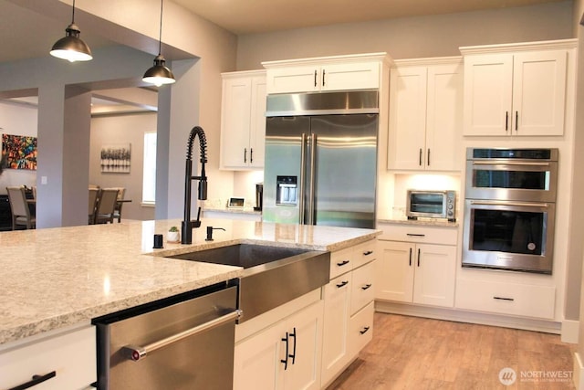 kitchen featuring a sink, hanging light fixtures, light wood-style floors, appliances with stainless steel finishes, and white cabinetry