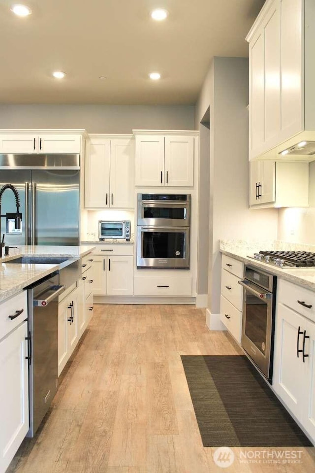 kitchen with light stone counters, light wood-style flooring, recessed lighting, appliances with stainless steel finishes, and white cabinetry