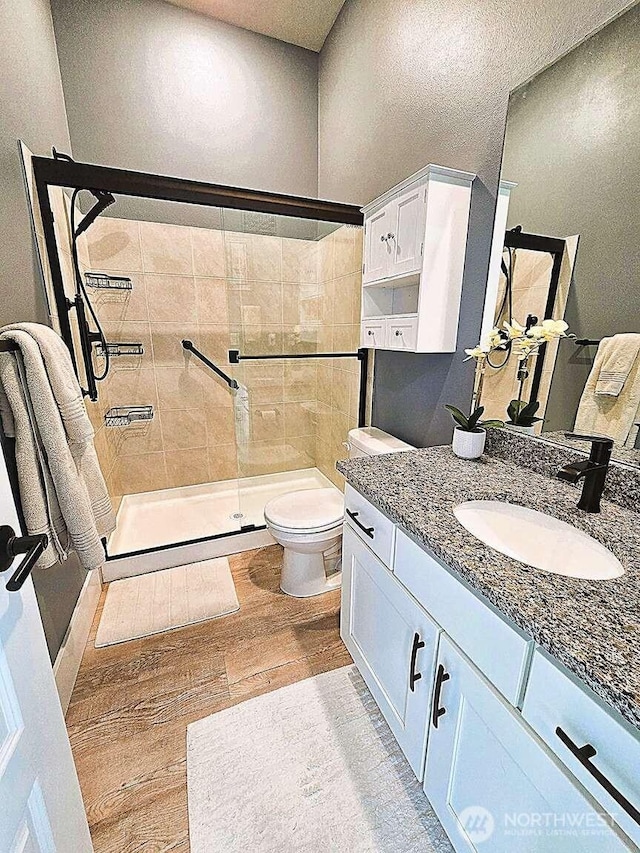 bathroom featuring a stall shower, toilet, vanity, and wood finished floors