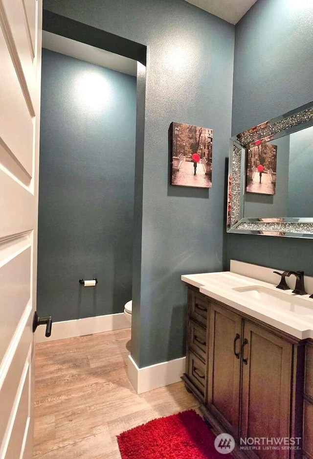 half bathroom featuring baseboards, toilet, wood finished floors, and vanity