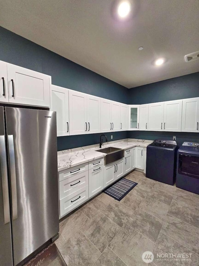 kitchen with light stone counters, freestanding refrigerator, a sink, white cabinets, and glass insert cabinets