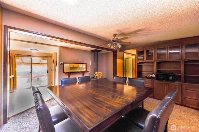 dining area with a ceiling fan, light colored carpet, and a textured ceiling