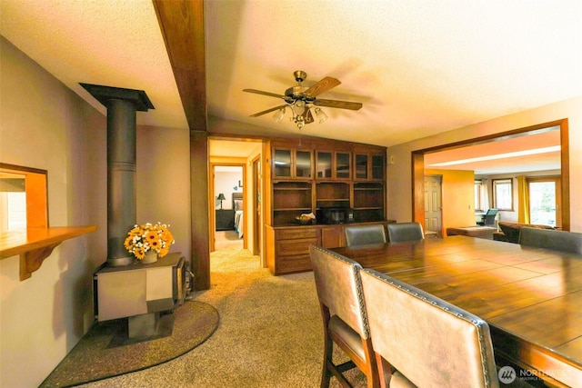 dining space featuring carpet flooring, a textured ceiling, a wood stove, and a ceiling fan