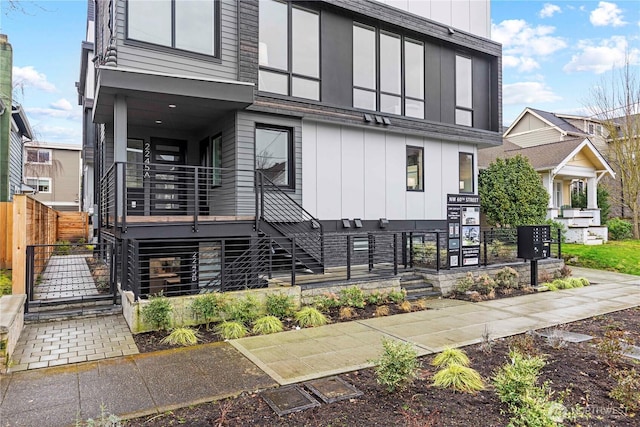 contemporary home featuring stairway, stone siding, board and batten siding, and fence