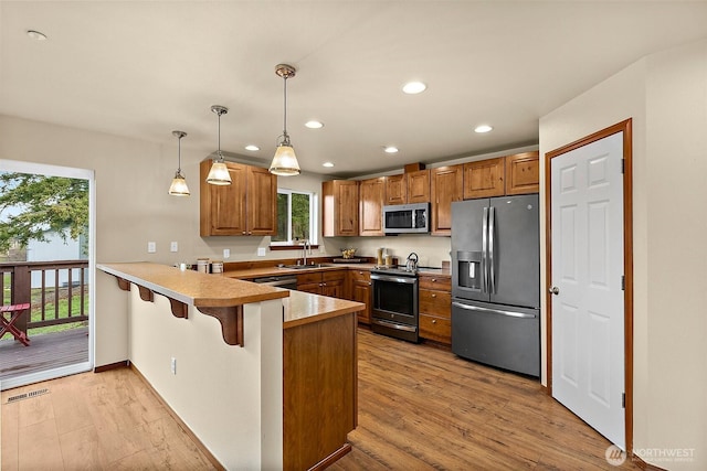 kitchen with a peninsula, light wood-type flooring, appliances with stainless steel finishes, and a sink