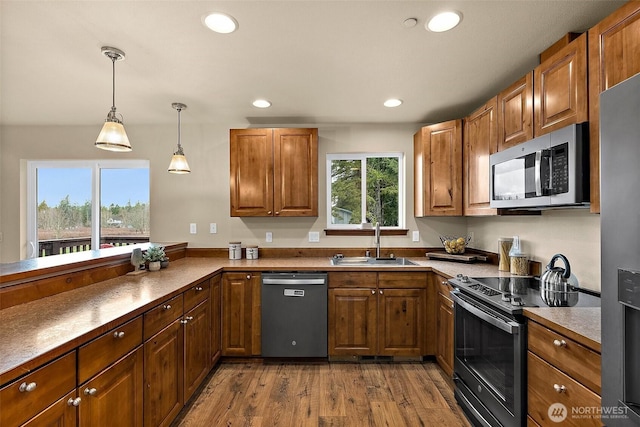 kitchen with wood finished floors, recessed lighting, a sink, stainless steel appliances, and brown cabinets