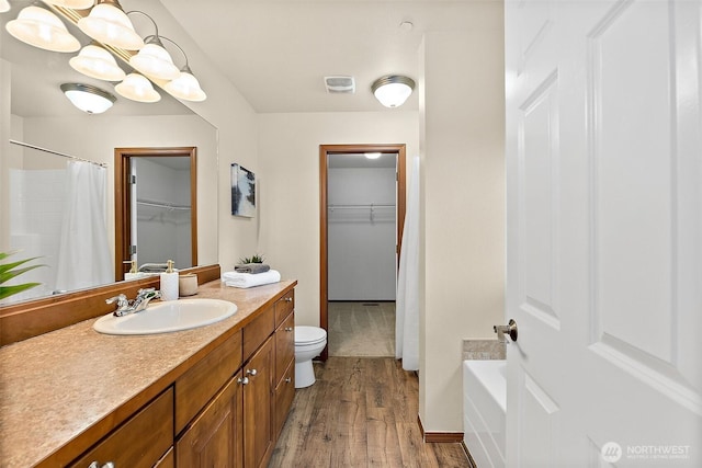 full bathroom with toilet, a spacious closet, wood finished floors, and vanity