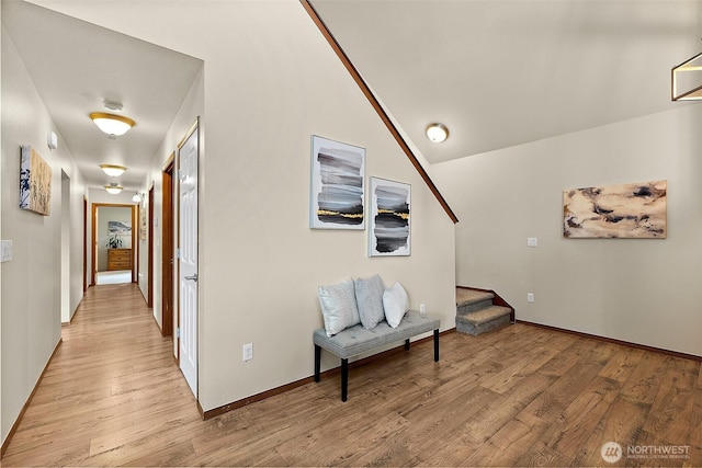 hallway featuring lofted ceiling, stairway, light wood-style flooring, and baseboards