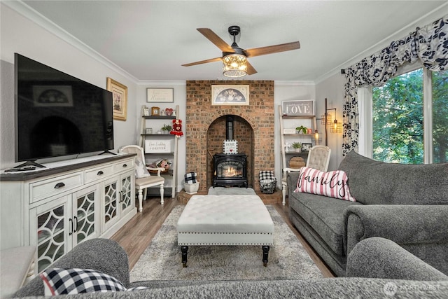 living room with crown molding, a wood stove, light wood-style floors, and ceiling fan